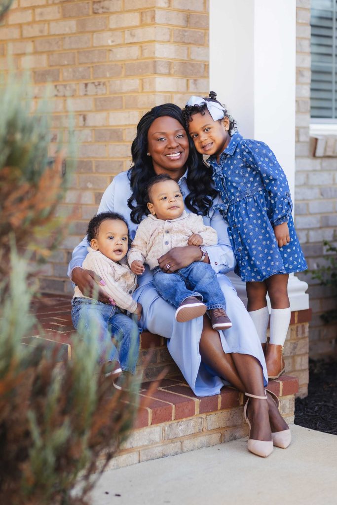 A black woman poses with her family on the steps of their home for a portrait.