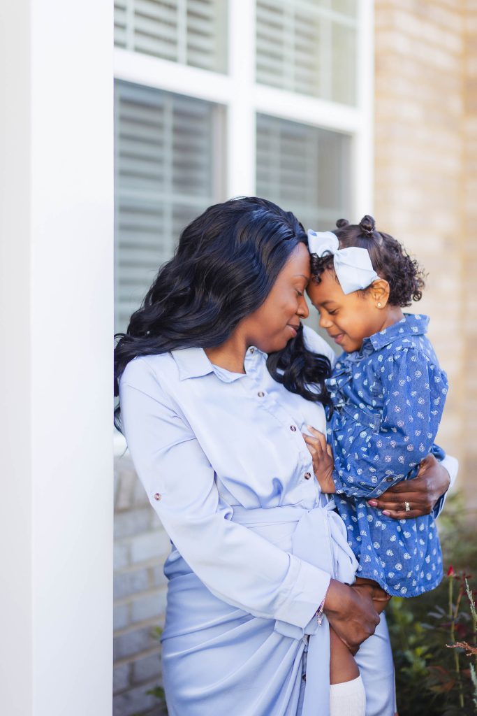 A family portrait of a pregnant woman holding her daughter at home.