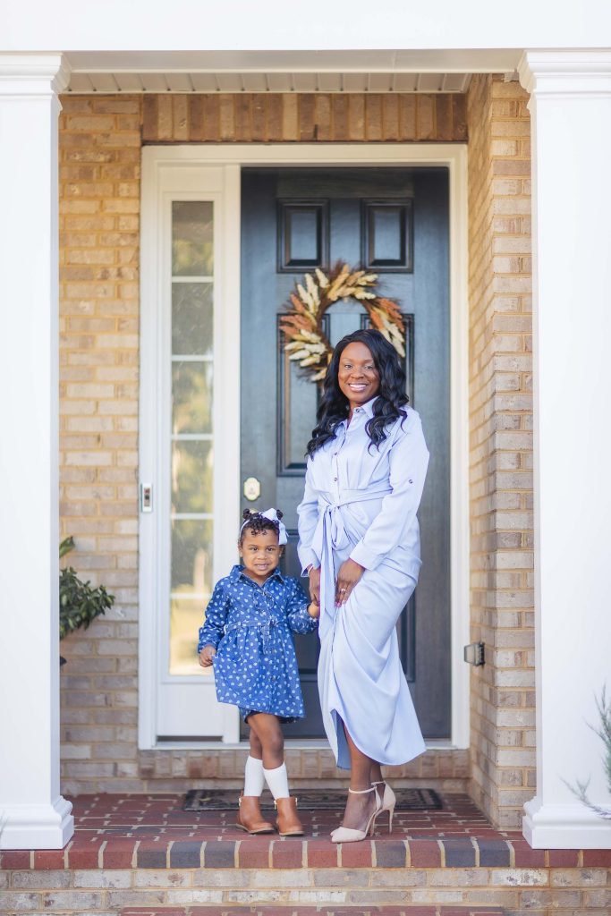 A mother and daughter posing for family portraits at home in front of a front door.