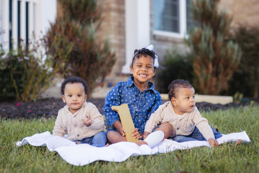 Three babies sitting on a blanket for family portraits at home.