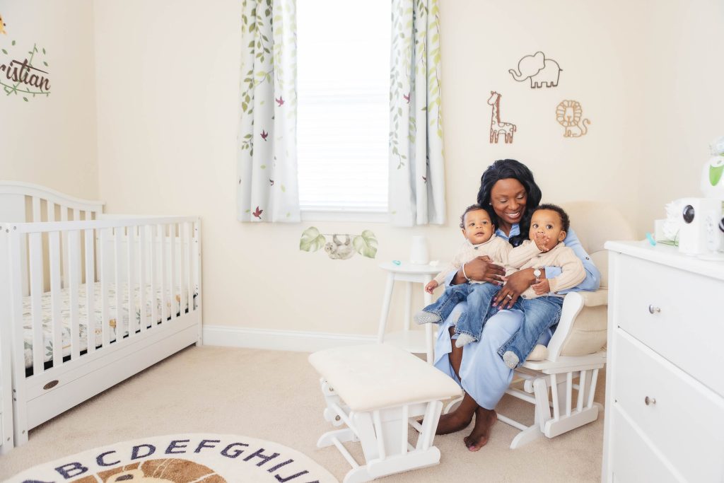 A woman is sitting in a rocking chair at home, surrounded by family portraits in a baby's room.