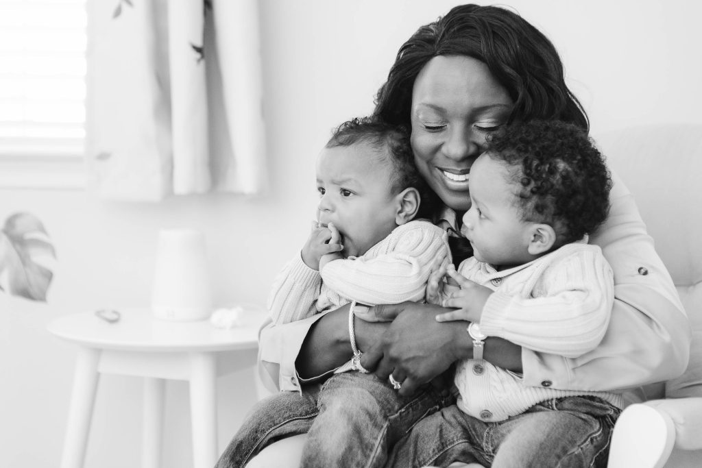 A black and white photo of a woman holding two babies, capturing a tender family moment at home.