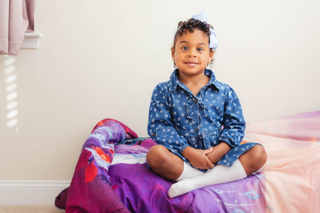 A little girl sitting on top of a bed at home.