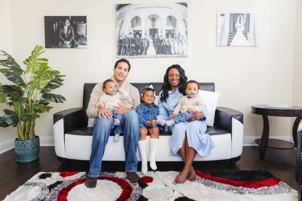 A family sits at home on a couch in a living room.