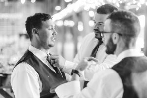 A black and white photo of a groom adjusting his tie.