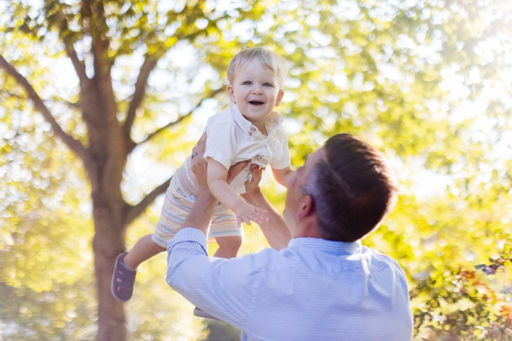 A family is capturing beautiful portraits at Quiet Waters Park, as a man lovingly holds a baby in the air.