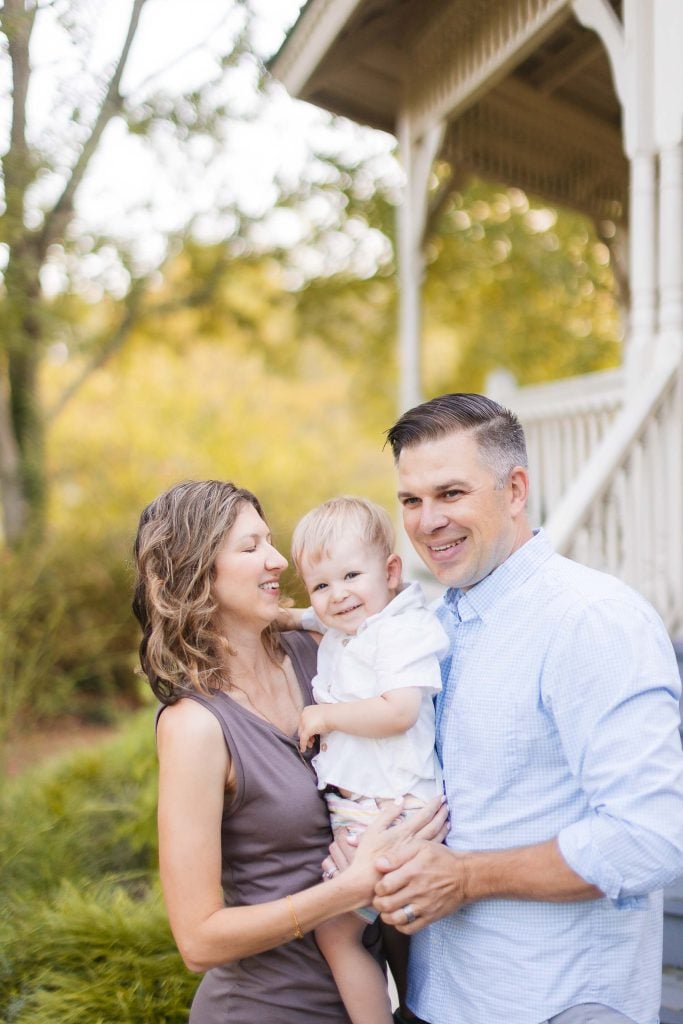 A family portrait at Quiet Waters Park, with a man and woman holding a baby in front of a porch.