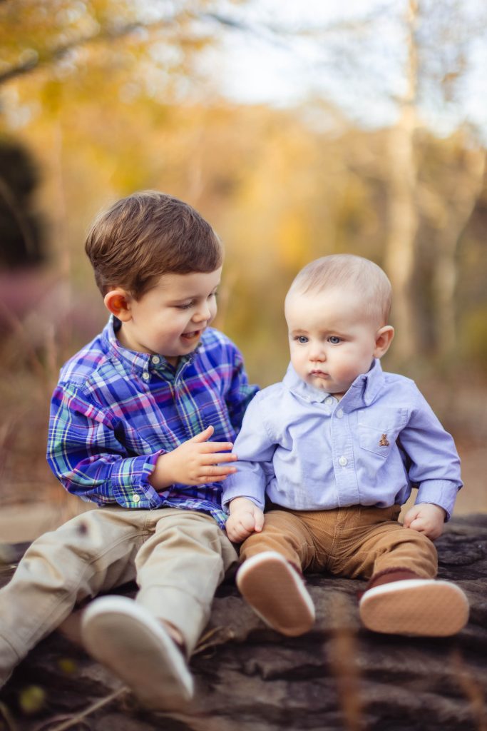 Family portrait of two boys sitting on a log in Annapolis, Maryland during the fall season.