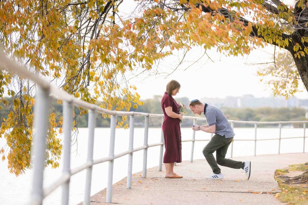 A man is kneeling on a bridge in Washington DC to surprise propose to his girlfriend.