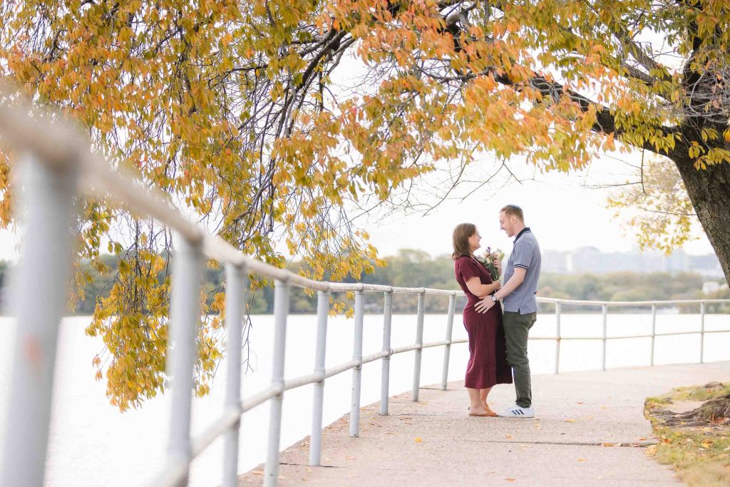 A couple is standing on a boardwalk near a river in Washington DC when a Surprise Wedding Proposal happens.