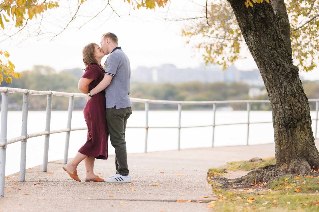 An engaged couple, having a wedding proposal, kissing on a bridge near the Surprise water.