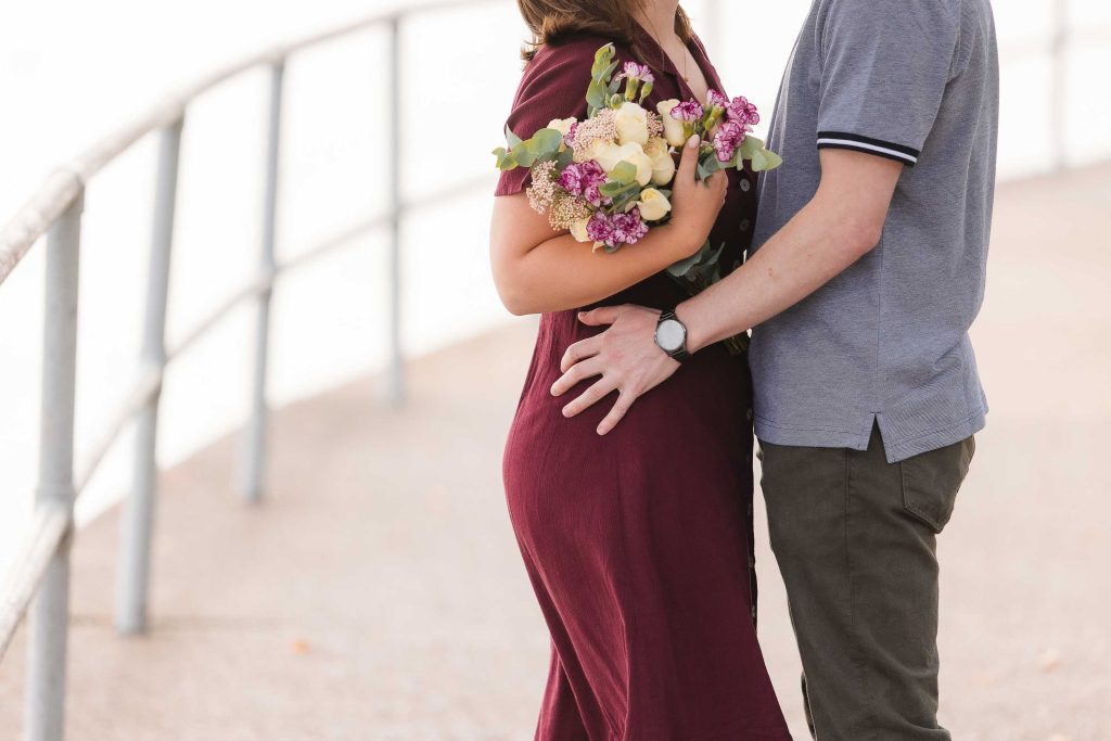 A couple in Washington DC shares a surprise wedding proposal on a bridge while holding bouquets.
