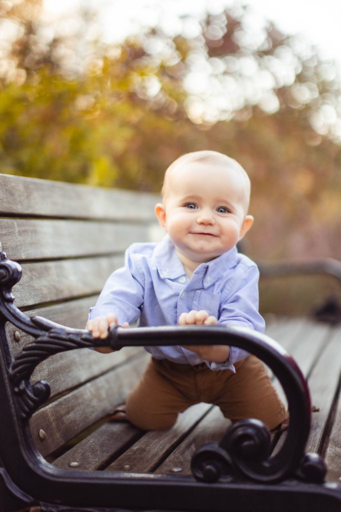 A baby is sitting on a bench in a park in Annapolis, Maryland, while their family takes portraits.