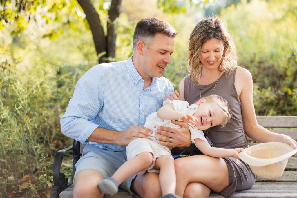 A family sits on a bench at Quiet Waters Park with a baby in a basket, creating beautiful portraits in Annapolis.