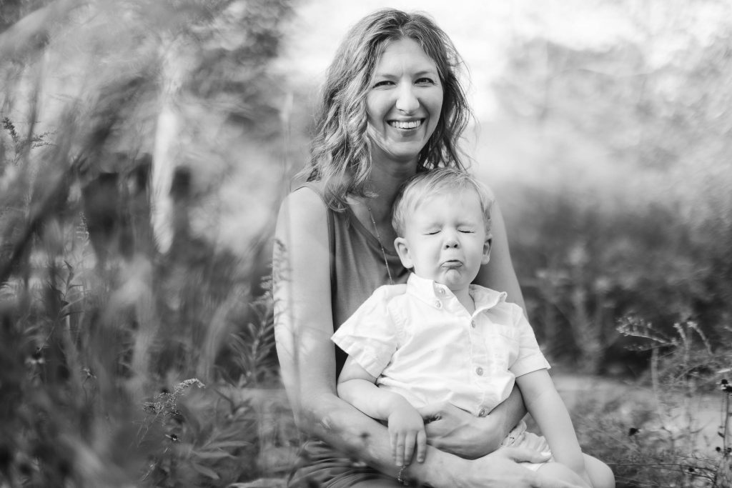 A black and white portrait of a woman holding a baby in the grass at Quiet Waters Park, Annapolis.