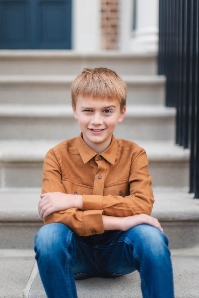 A boy in a brown shirt sits on the steps of a Belair Mansion.