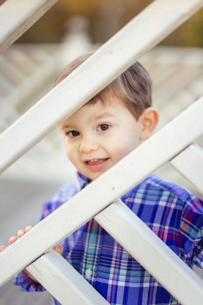 A young boy from Annapolis, Maryland peeking through a wooden fence at Quiet Waters Park with his family.