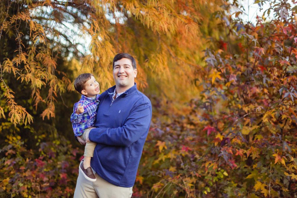 A man holding a child in front of fall foliage at Quiet Waters Park in Annapolis, Maryland.