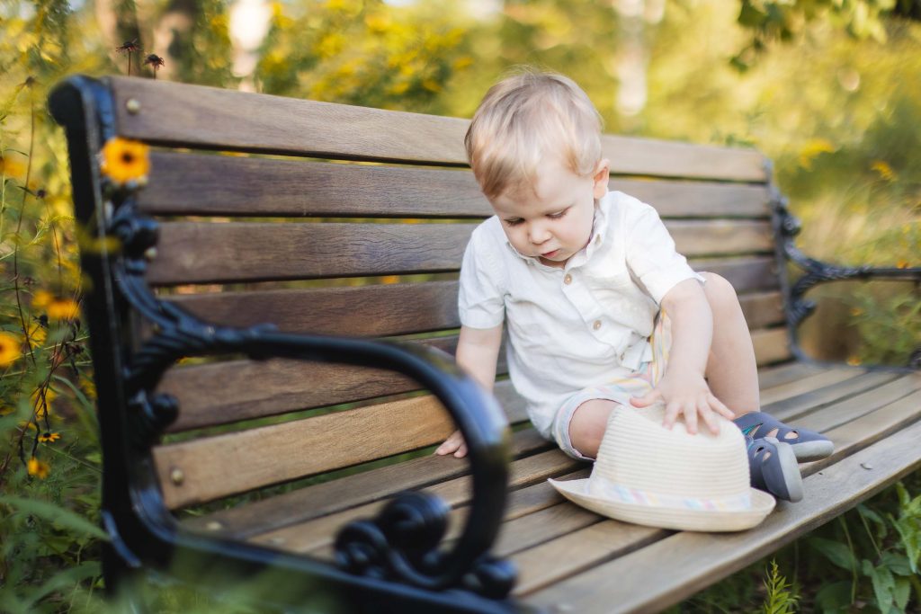 A toddler sitting on a wooden bench in Annapolis, wearing a hat, for family portraits.