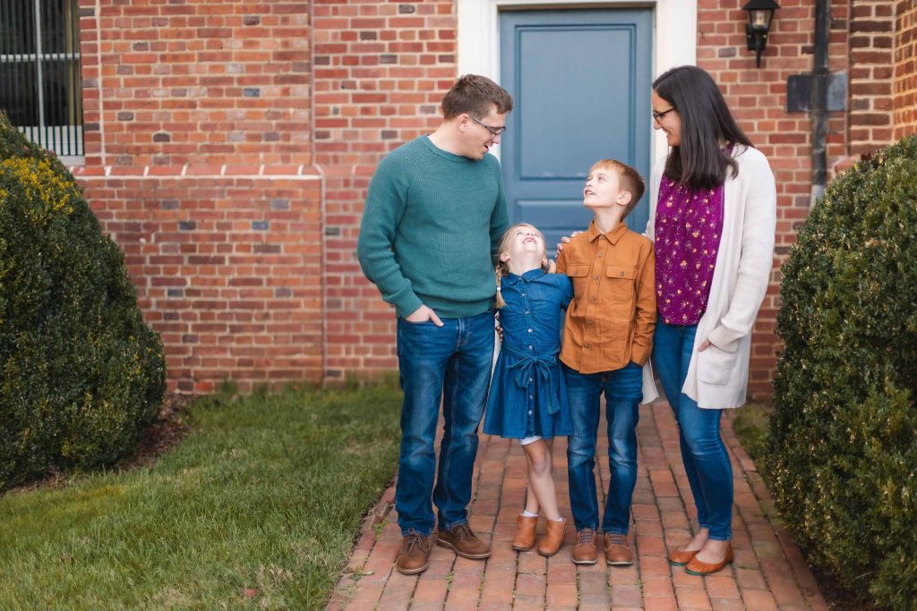 A Family is standing in front of a brick house, posing for Portraits.