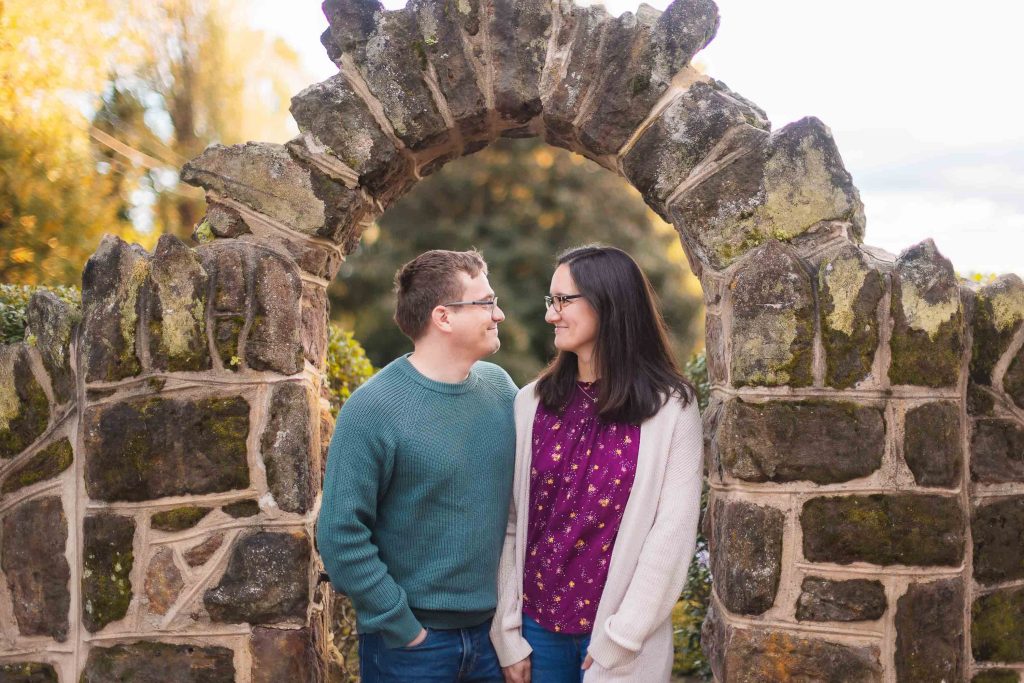 An engaged couple posing for portraits in front of the stone archway at Belair Mansion.