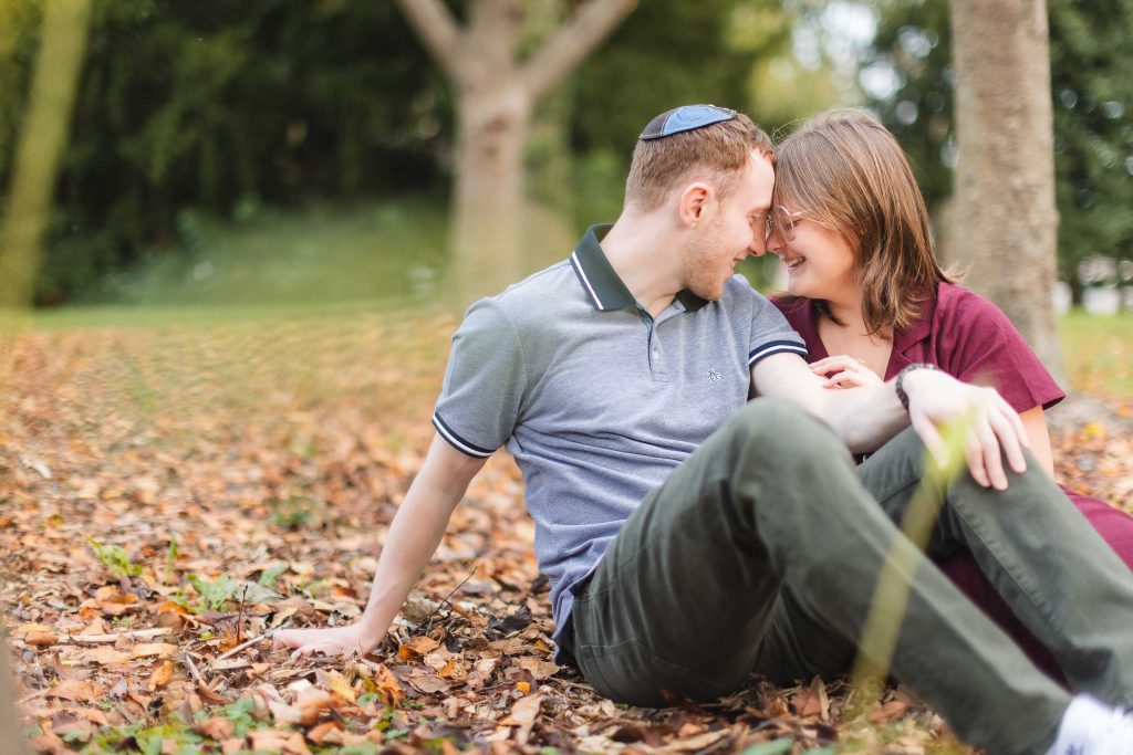 A couple sits on the ground in the autumn leaves, completely unaware of the Surprise unfolding around them.