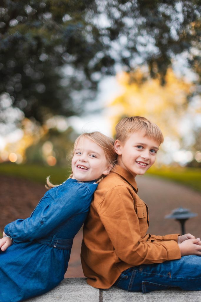 Two children sitting on a bench in a park for a family portrait.