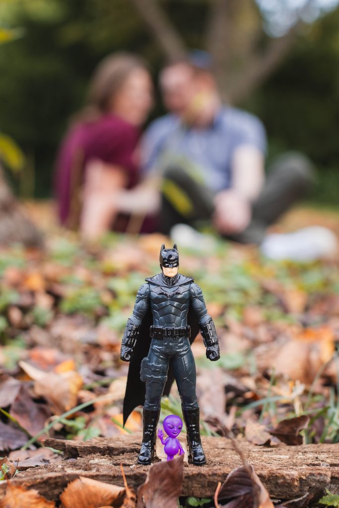 A batman figurine sits on a pile of leaves in front of a couple, adding an element of surprise.