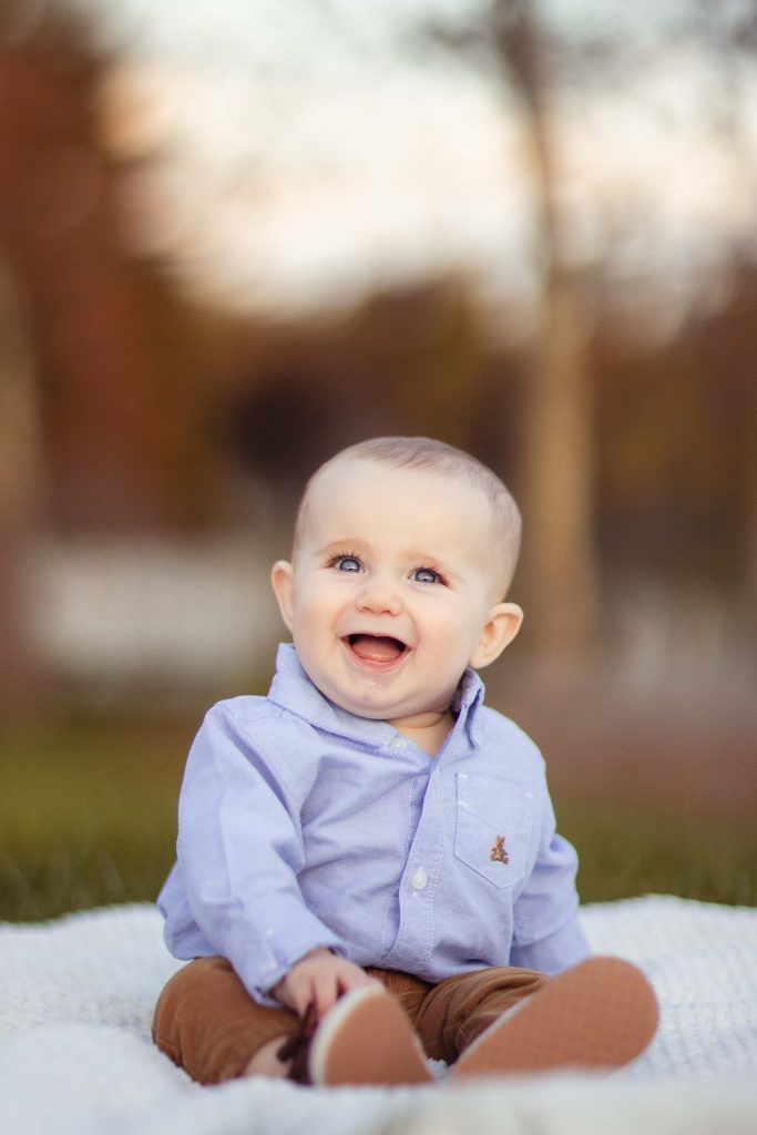A baby sits on a blanket at Quiet Waters Park and smiles.