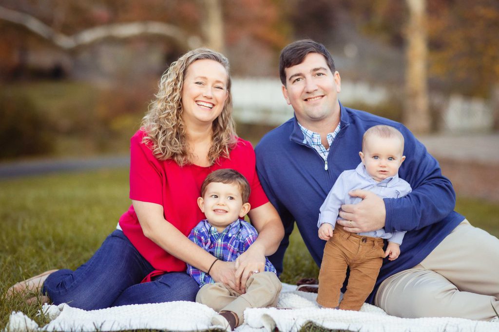 A Family in Annapolis, Maryland sits on the grass and poses for a photo.