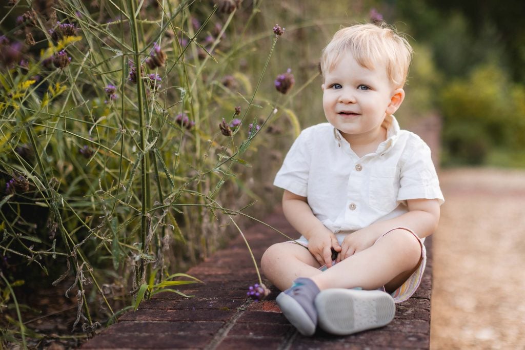 A toddler sitting on a brick wall in a Quiet Waters Park garden.