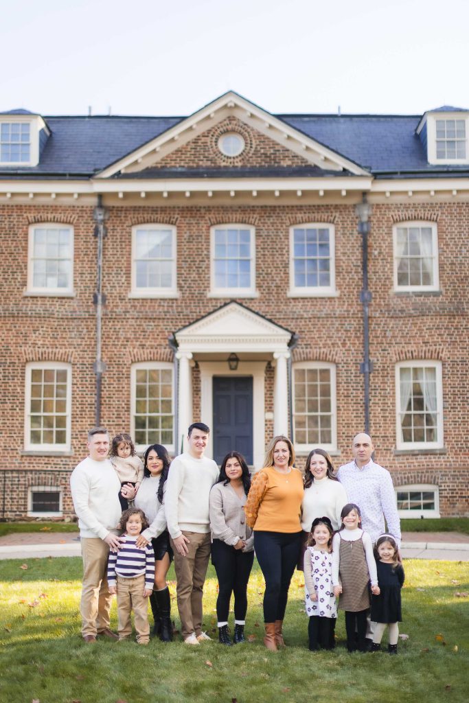 A large family group stands on a lawn in front of the impressive, two-story Belair Mansion, capturing a timeless portrait.
