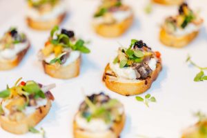 Close-up of assorted bruschetta appetizers topped with cream, vegetables, microgreens, and garnishes—perfect for a Baltimore wedding or an elegant event near the National Aquarium.