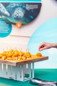 A hand reaches for a skewered appetizer from a tray on a table, with an aquarium-themed display and sea turtle image in the background—capturing the elegant details of a Baltimore wedding celebration.