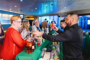 At a busy reception at the National Aquarium in Baltimore, a bartender serves drinks, including a can of Coca-Cola, to guests with bottles and mixers visible on the counter.