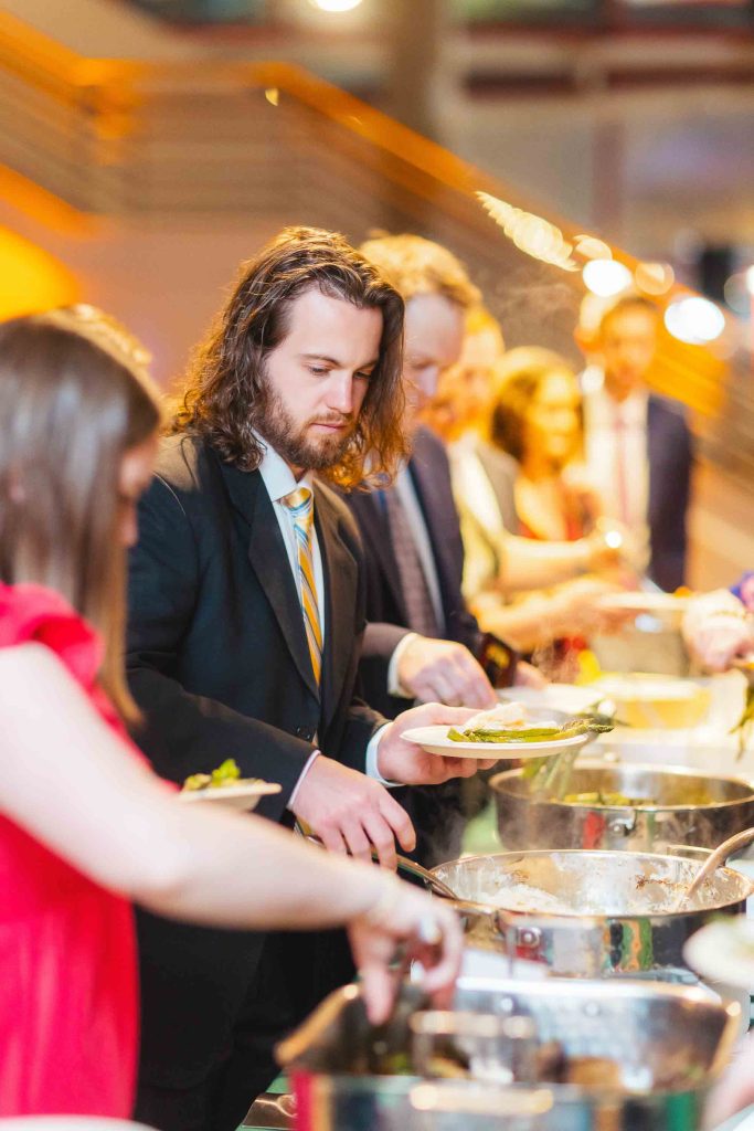 Guests in formal attire serve themselves food from a buffet line at an indoor reception near Baltimore’s National Aquarium.