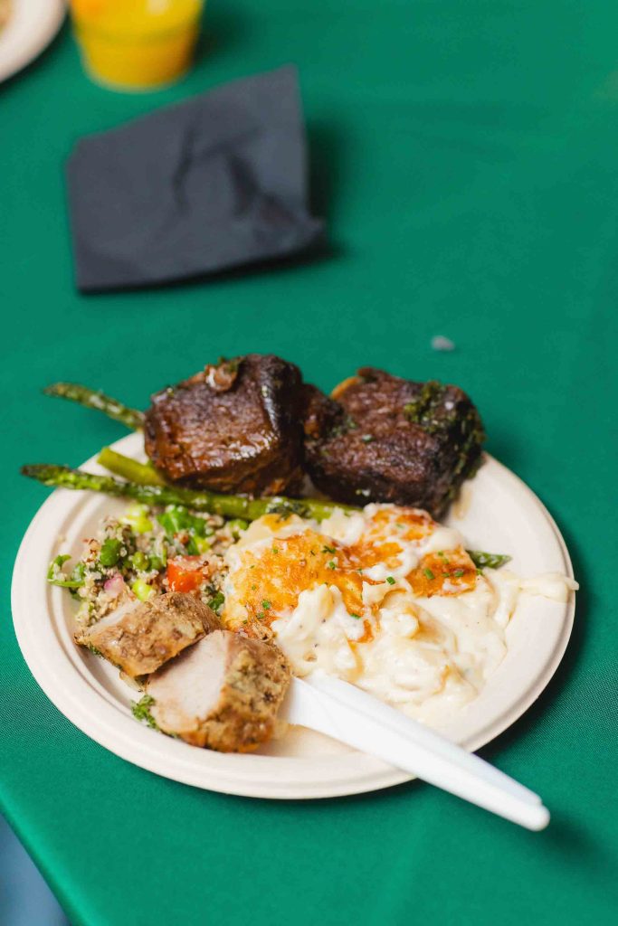 A plate with grilled meat, stuffed chicken, macaroni and cheese, asparagus, and vegetable salad sits on a green tablecloth in Baltimore—capturing the delicious details of a wedding feast. A white plastic fork rests invitingly on the plate.