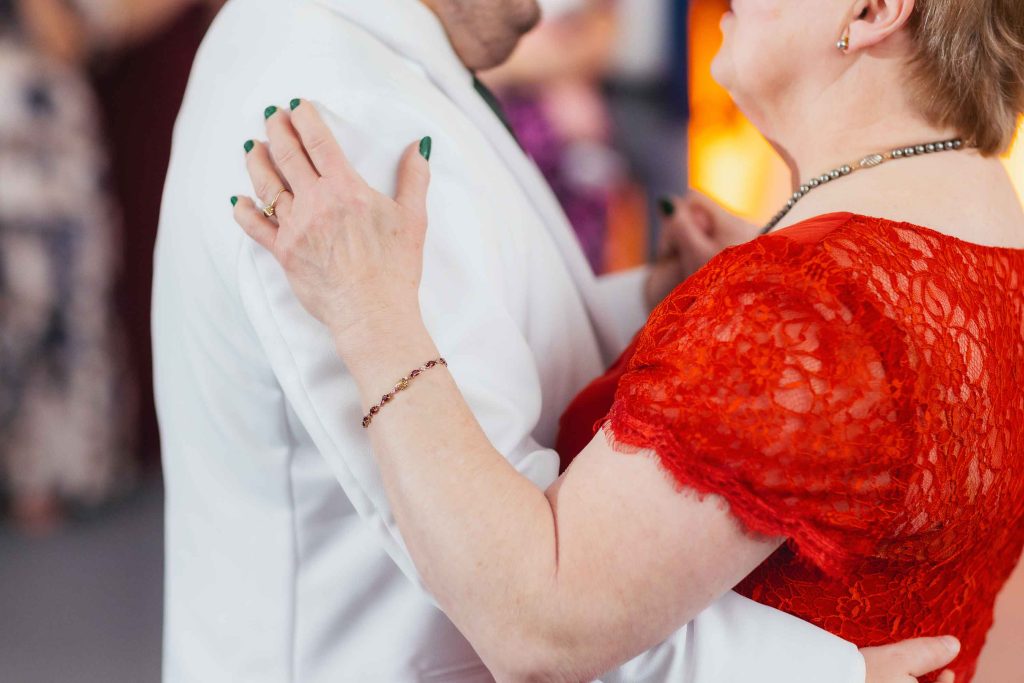 At a lively reception in Baltimore, two people dance closely; one in a white suit, the other in a red lace dress with green nail polish. Their faces are not fully visible, capturing an intimate moment at the National Aquarium.