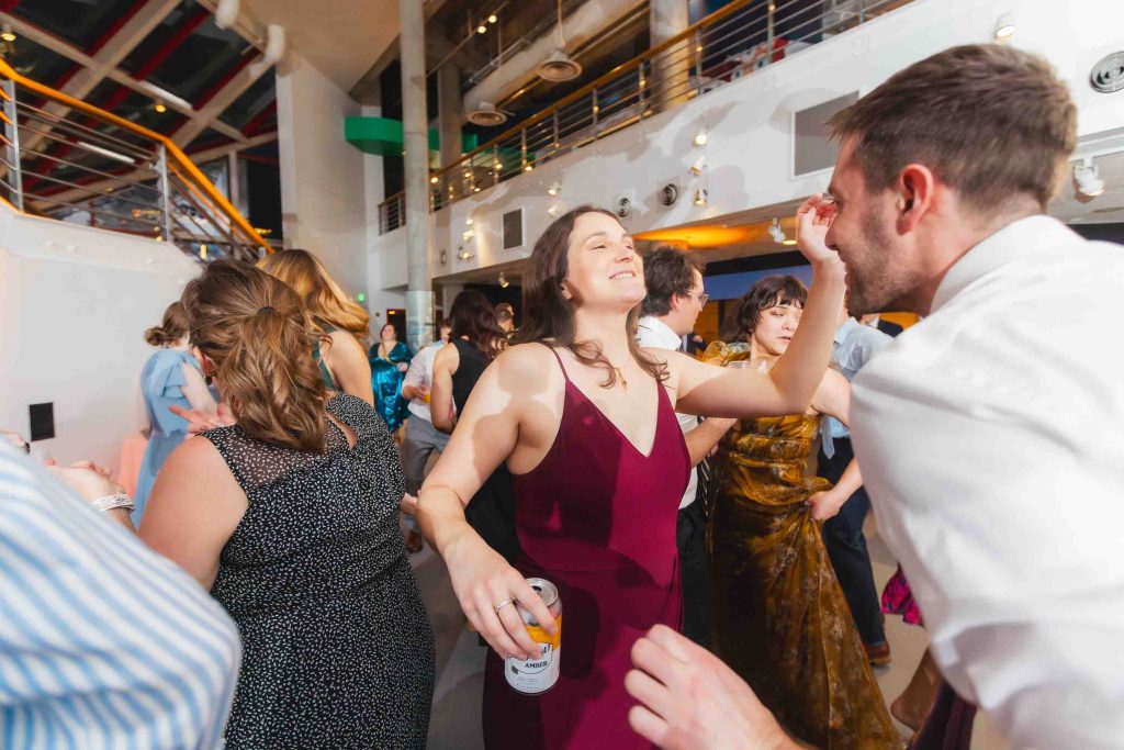 A group of people dance and mingle at a Baltimore wedding reception; a woman in a burgundy dress smiles while reaching toward a man in a white shirt.